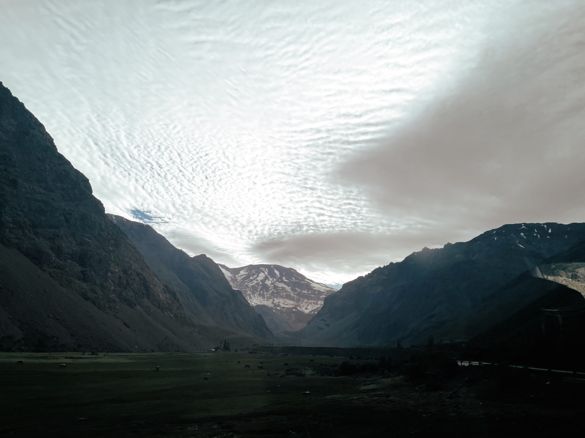 Vista de um vale em meio às montanhas dos Andes. Ao fundo, um vulcão