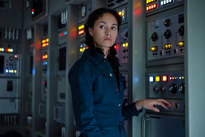 Uma andróide perto de um painel cheio de botões e alavancas